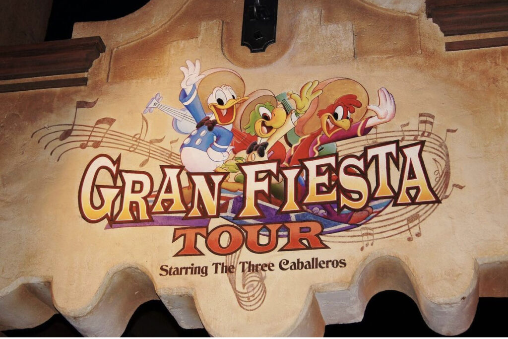 Promotional wall graphic for 'Gran Fiesta Tour Starring The Three Caballeros' featuring animated characters Donald Duck, Jose Carioca, and Panchito Pistoles, set against a stylized musical note background.